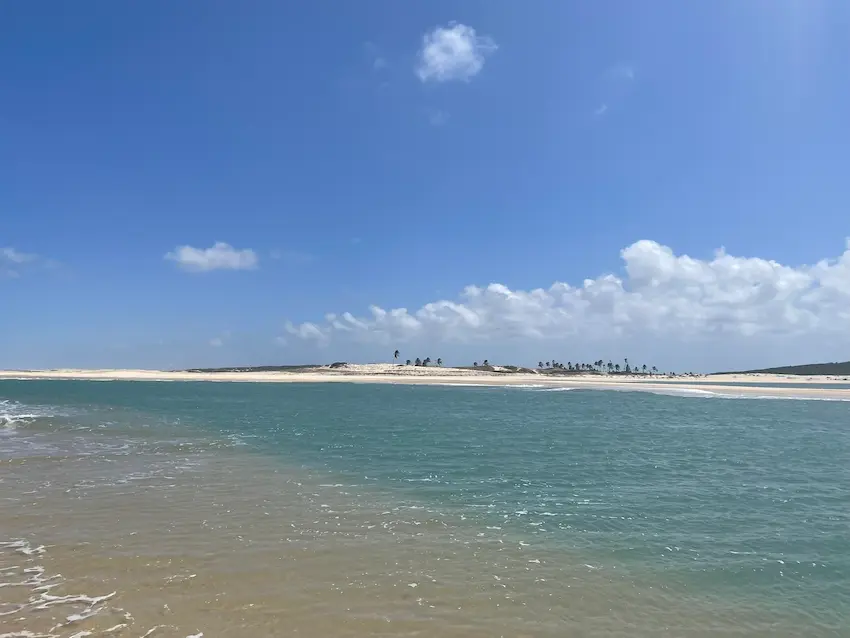 Praia paradisíaca em Águas Belas, a 65 km do Refúgio Hostel Fortaleza, onde o rio se encontra com o mar sob um céu ensolarado, formando piscinas naturais e um cenário tranquilo