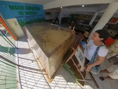 A foto registra a famosa maior rapadura do mundo, exposta no Engenho Complexo Tradição, uma parada imperdível durante o passeio para Águas Belas, organizado pelo Refúgio Hostel Fortaleza & Pousada. Com seu imenso bloco de rapadura em destaque, o complexo é uma verdadeira imersão na cultura e tradição nordestina. Os visitantes têm a chance de conhecer mais sobre a produção artesanal de rapadura e outros doces típicos, além de aproveitar para levar lembranças saborosas para casa. Esse é mais um momento especial que faz parte da experiência completa oferecida aos nossos hóspedes, unindo conhecimento, cultura e sabores inesquecíveis.
